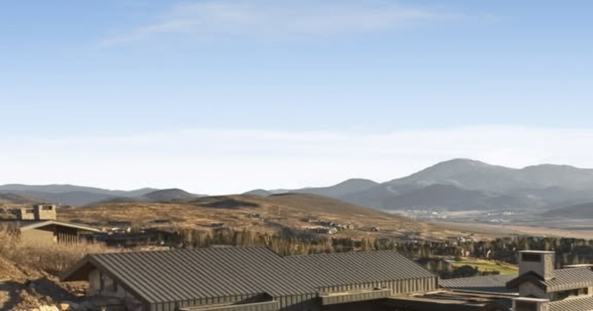 Dark metal rooftops below brown hills and distant mountains